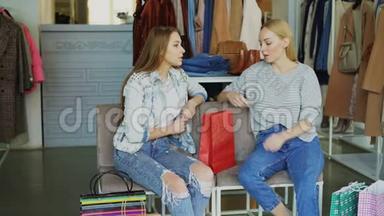 两位年轻女士坐在商场的服装部，购物后聊天。 多彩女`衣服和